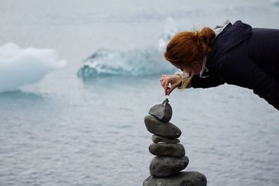 Woman making stack of stones against sea