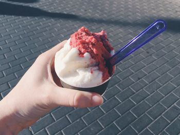 Cropped hand of woman holding ice cream cup against footpath in city during summer