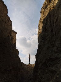 Low angle view of man standing on rock against sky