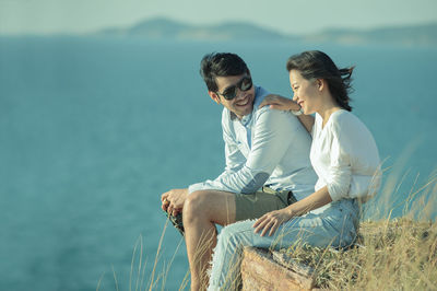 Smiling man and woman sitting against sea at beach