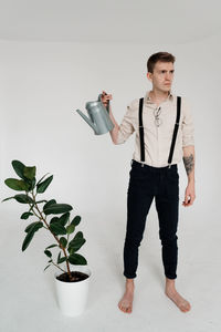 Young man looking away while standing on potted plant against wall