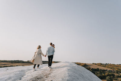 Rear view of friends on rock against clear sky