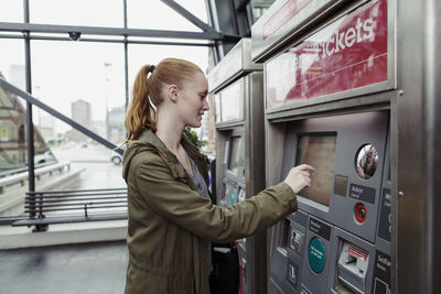 Side view of woman using ticket machine at railroad station