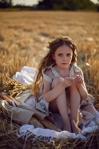 Girl child sitting on a mown wheat field at sunset with bread