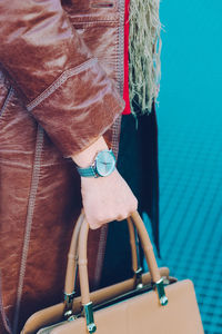 Midsection of woman with bag standing against blue wall