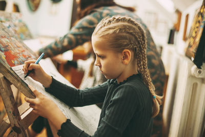 Beautiful teenage girl with pigtails at art school draws graphics with pen on easel