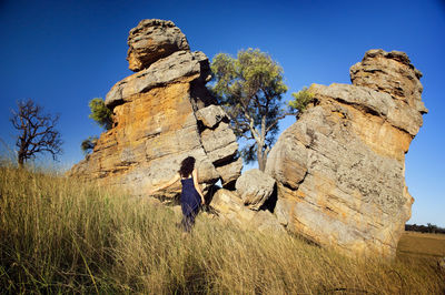 Rear view of woman standing by rock formation against blue sky