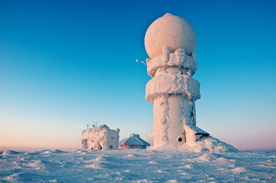 Snow covered built structure against clear blue sky during sunset