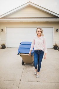 Portrait of woman with garbage bin walking on footpath