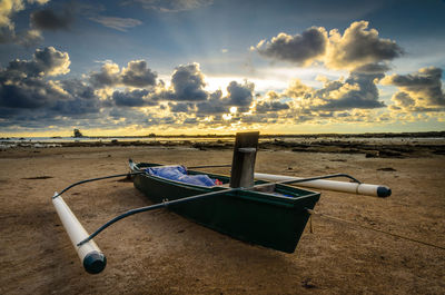 Outrigger moored at beach against cloudy sky during sunset