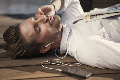 Businessman listening music while lying on boardwalk