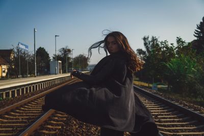 Woman sitting on railroad track against sky