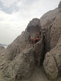 Man sitting on rock by mountains against sky