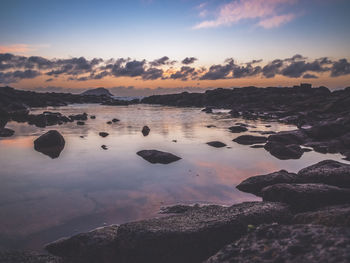 Colors of sunrise seen from a rocky beach with cloud reflections in the sea water