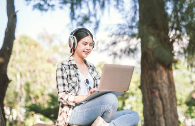 Young woman using phone while sitting on tree trunk