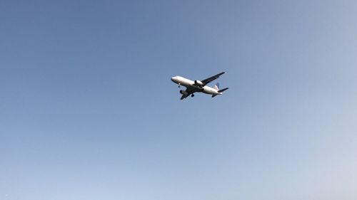 Low angle view of airplane flying against clear blue sky