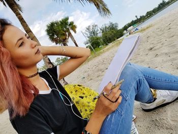 Young woman with note pad sitting on sand