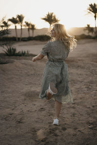 Cheerful woman dancing on beach while looking away during sunset