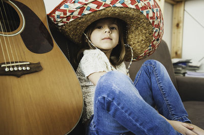 Portrait of girl wearing hat while sitting by string instrument