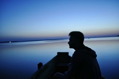 Rear view of silhouette man sitting against sea