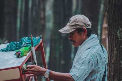 Side view of man holding tree trunk in forest