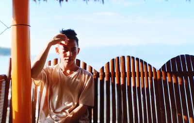 Portrait of young man standing against fence