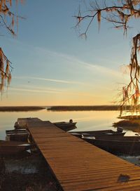 Boats moored by jetty in river against sky during sunset