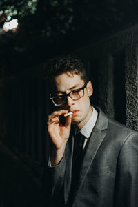 Businessman smoking cigarette by illuminated wall at night