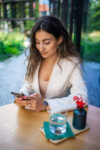 Young woman using mobile phone while sitting at table