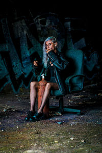 Woman smoking cigarette while sitting on chair against wall