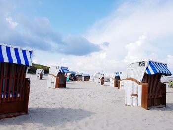 Hooded beach chairs on sand against sky