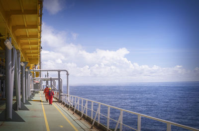 Man standing on railing by sea against sky