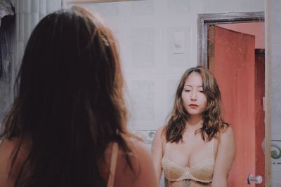 Young woman in bra standing against mirror