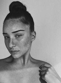 Close-up portrait of young woman with freckles against wall