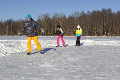 Teenage boy with girls ice-skating on snow outdoors