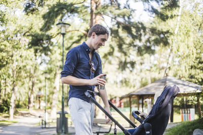 Smiling man holding drink while looking at baby in carriage on sunny day