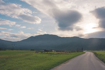 Empty road amidst field against sky