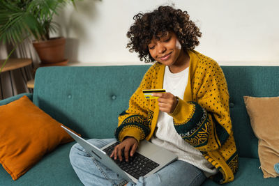 Young woman using laptop while sitting on sofa at home