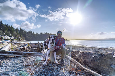 Man kneeling down with his pet great dane dog on northwest beach with bright sunshine and driftwood.