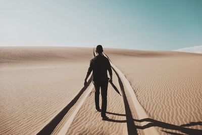 Rear view of man walking on desert against sky