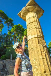 Low angle portrait of woman pointing at old column