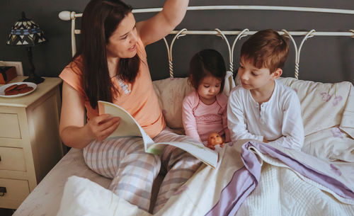 Close-up of mother telling bed time story to children on bed at home