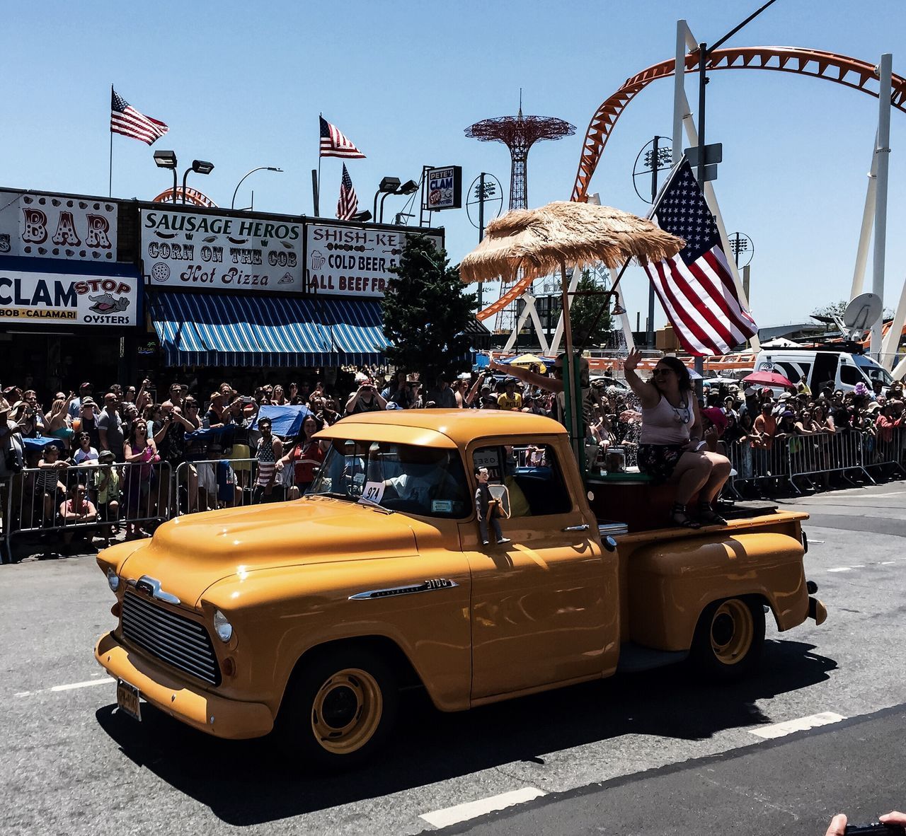 building exterior, built structure, architecture, city, clear sky, amusement park, amusement park ride, street, transportation, arts culture and entertainment, incidental people, land vehicle, car, day, mode of transport, outdoors, large group of people, sunlight, city life, sky