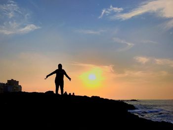 Silhouette woman with arms outstretched standing at beach against sky during sunset