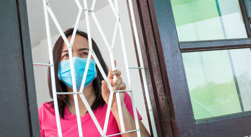 Low angel view of mature woman wearing flu mask standing by window