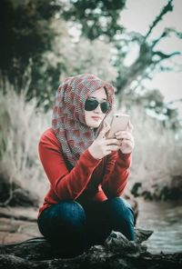 Woman wearing hijab using smart phone while sitting outdoors