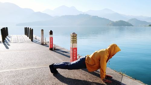 Man standing on sea by mountain against sky