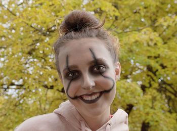 Portrait of smiling teenage girl with halloween make-up against plants