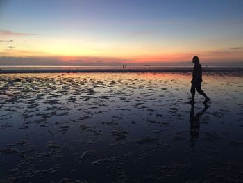 Silhouette man walking of wet beach against sky during sunset