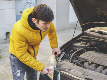 A young caucasian guy in a yellow jacket inspects an internal breakdown with an open car hood